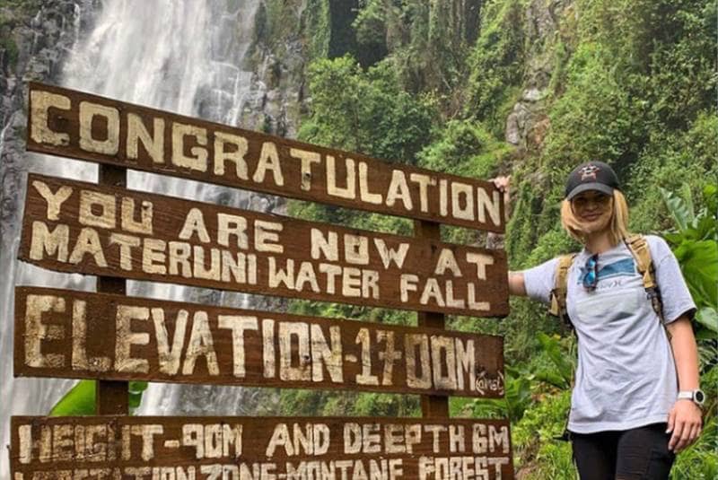Tourist at the Materuni Waterfall sign showing elevation of 1700m